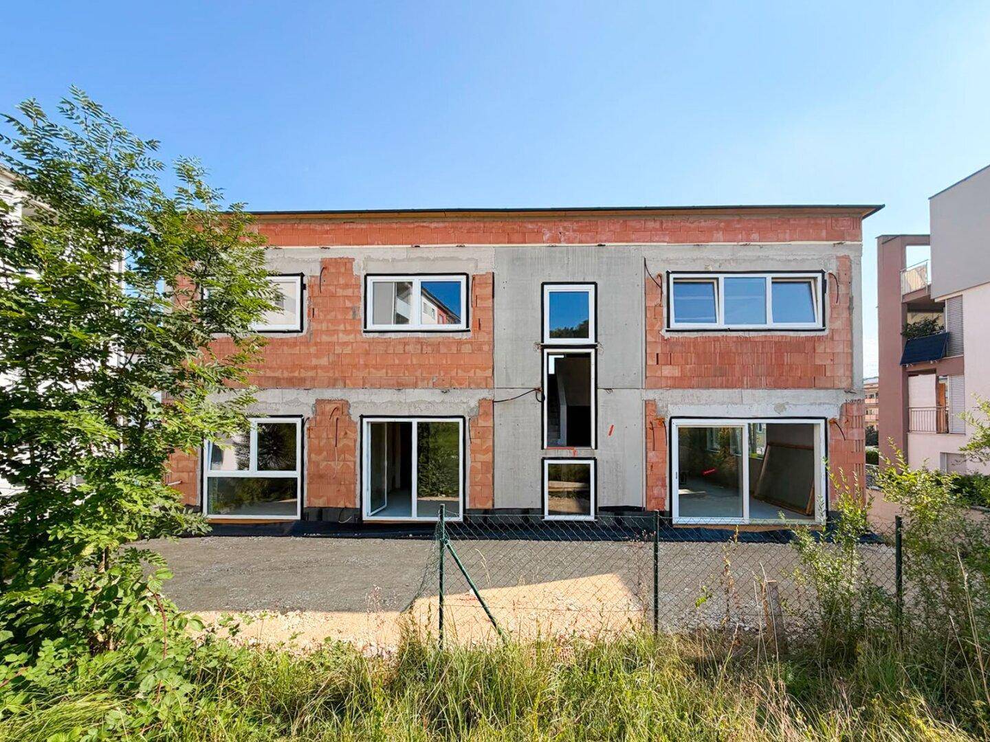 Rückansicht des Neubaus im Rohbau mit vielen Fenstern und Schiebetüren zum Gartenbereich.
