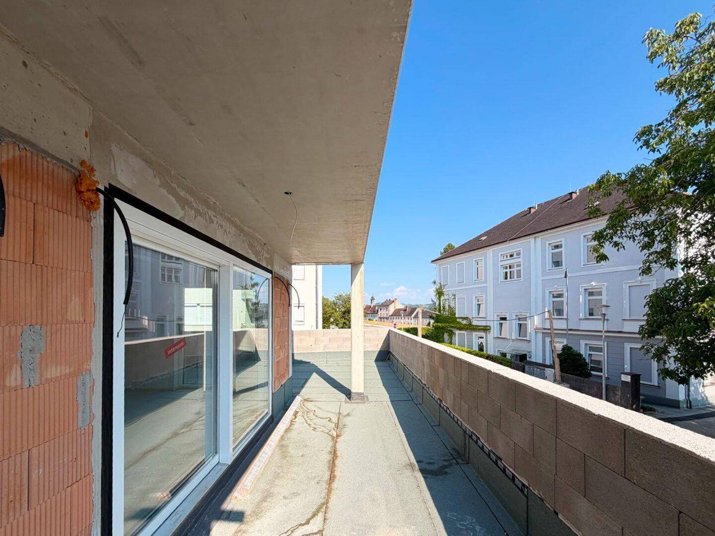 Balkon im Rohbau mit Blick auf die Nachbargebäude und den blauen Himmel.