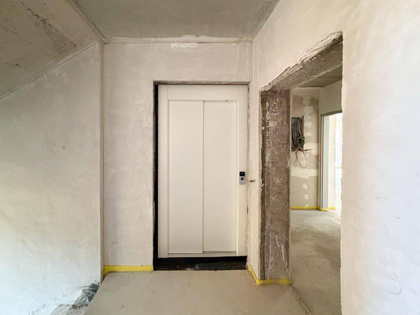 Innenbereich im Rohbau mit installiertem Aufzug und unfertigen Wänden.