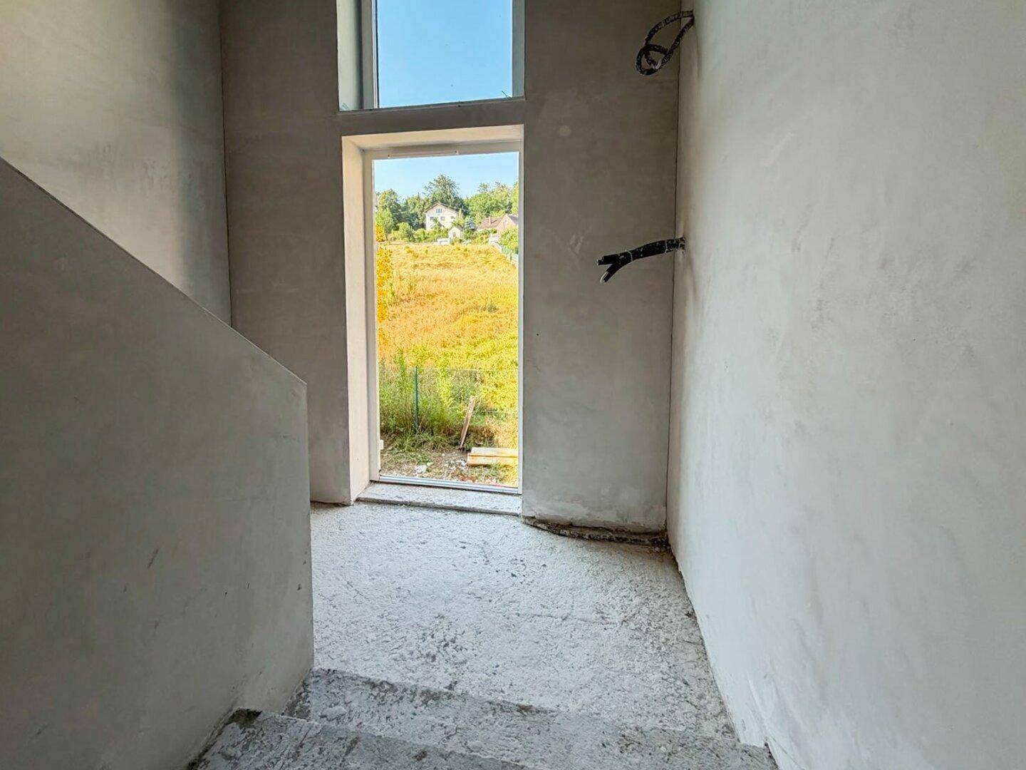 Treppenbereich im Rohbau mit Fenster und Blick auf die grüne Landschaft.