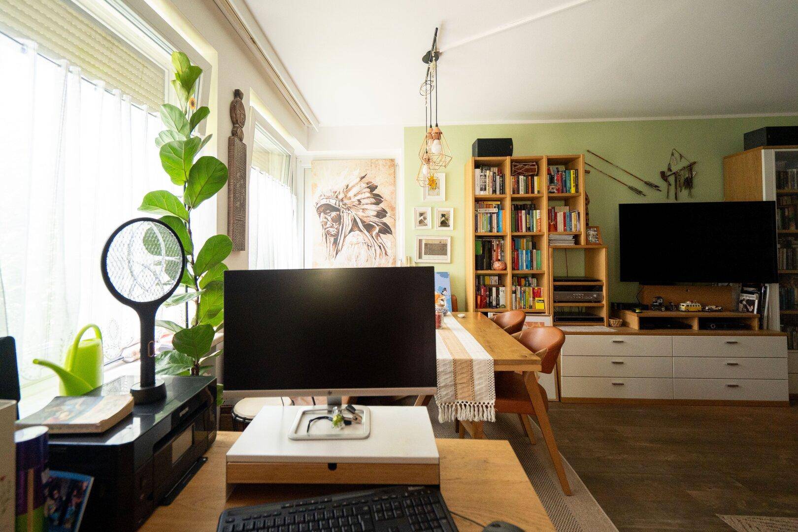 Lichtdurchfluteter Wohnbereich mit Arbeitsplatz, Esstisch und Blick auf die grüne Umgebung durch große Fenster.
