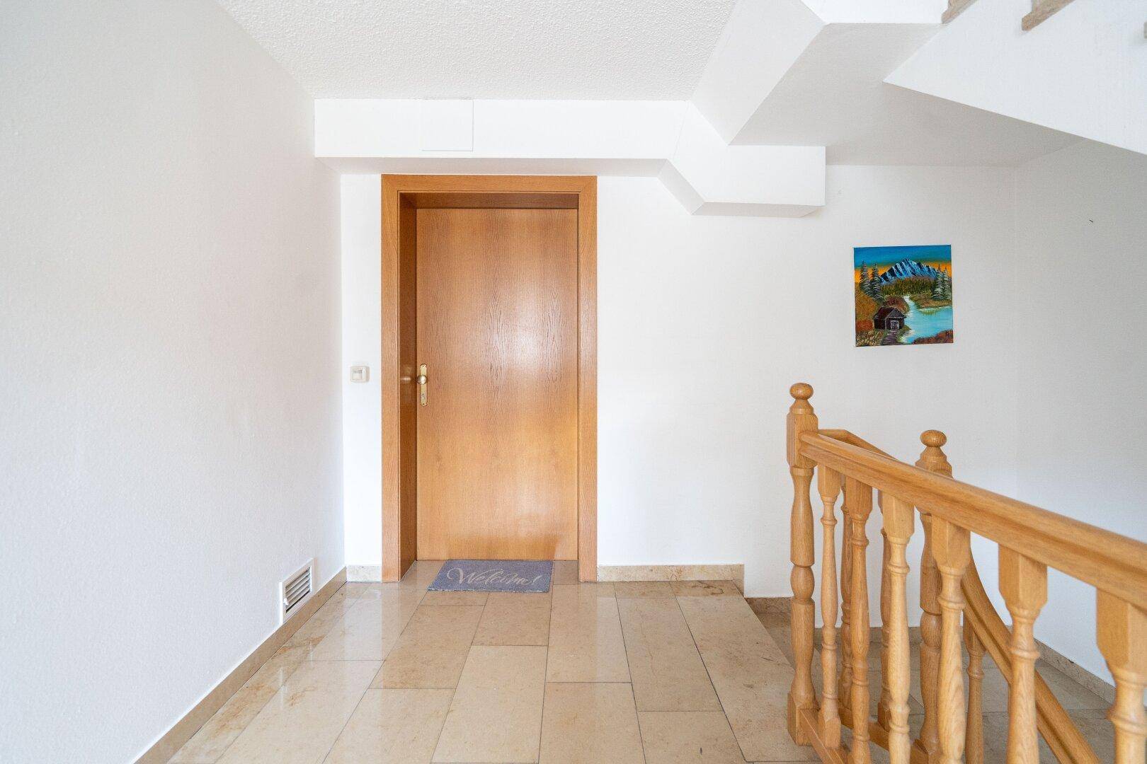 Heller Flur mit Treppenaufgang, Holztür und Fliesenboden, sauber und gepflegt.