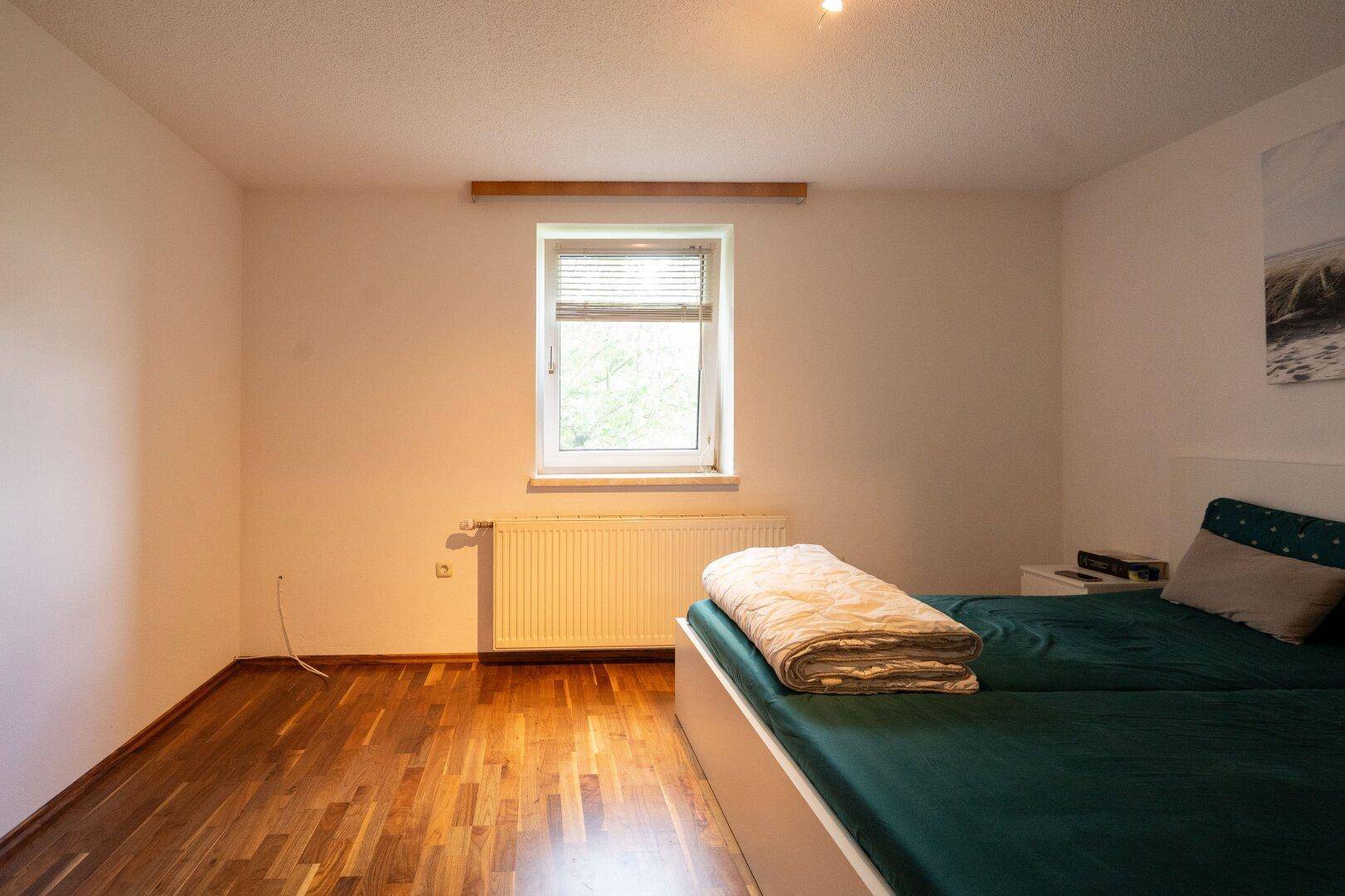 Helles Schlafzimmer mit Doppelbett, Holzboden und Fenster, einfach und gemütlich eingerichtet.