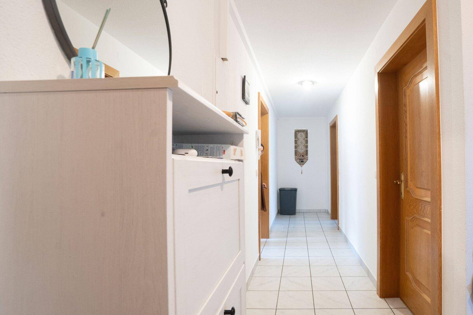 Langer, heller Flur mit Fliesenboden und Holztüren, ordentlich und gepflegt.