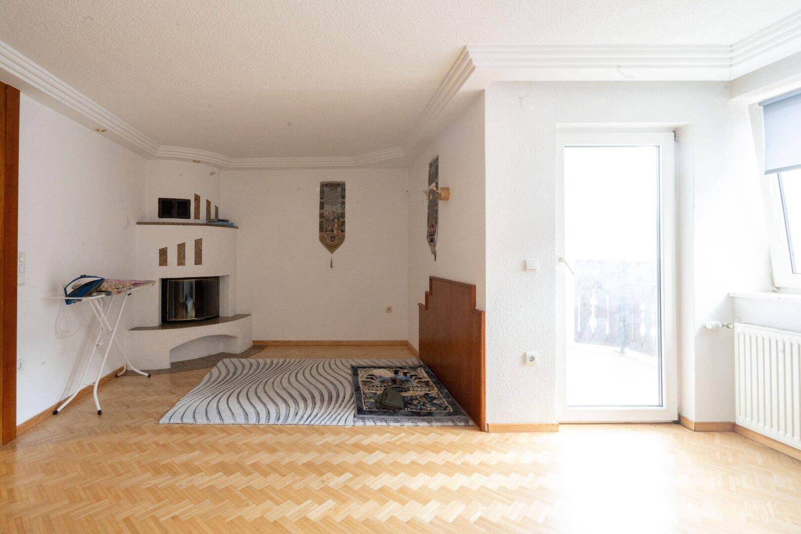 Helles Wohnzimmer mit Kamin, Parkettboden und Zugang zu einem Balkon, geräumig und einladend.