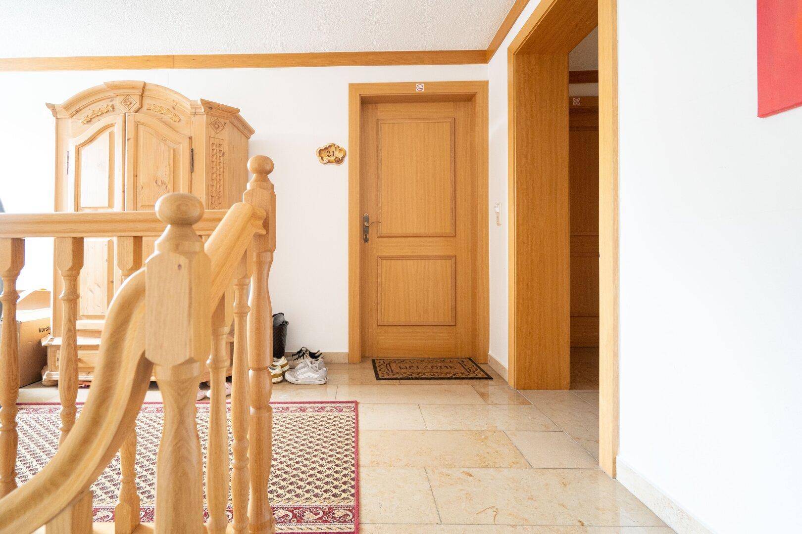 Heller Eingangsbereich mit Holztreppe, Fliesenboden und traditionellem Holzschrank.