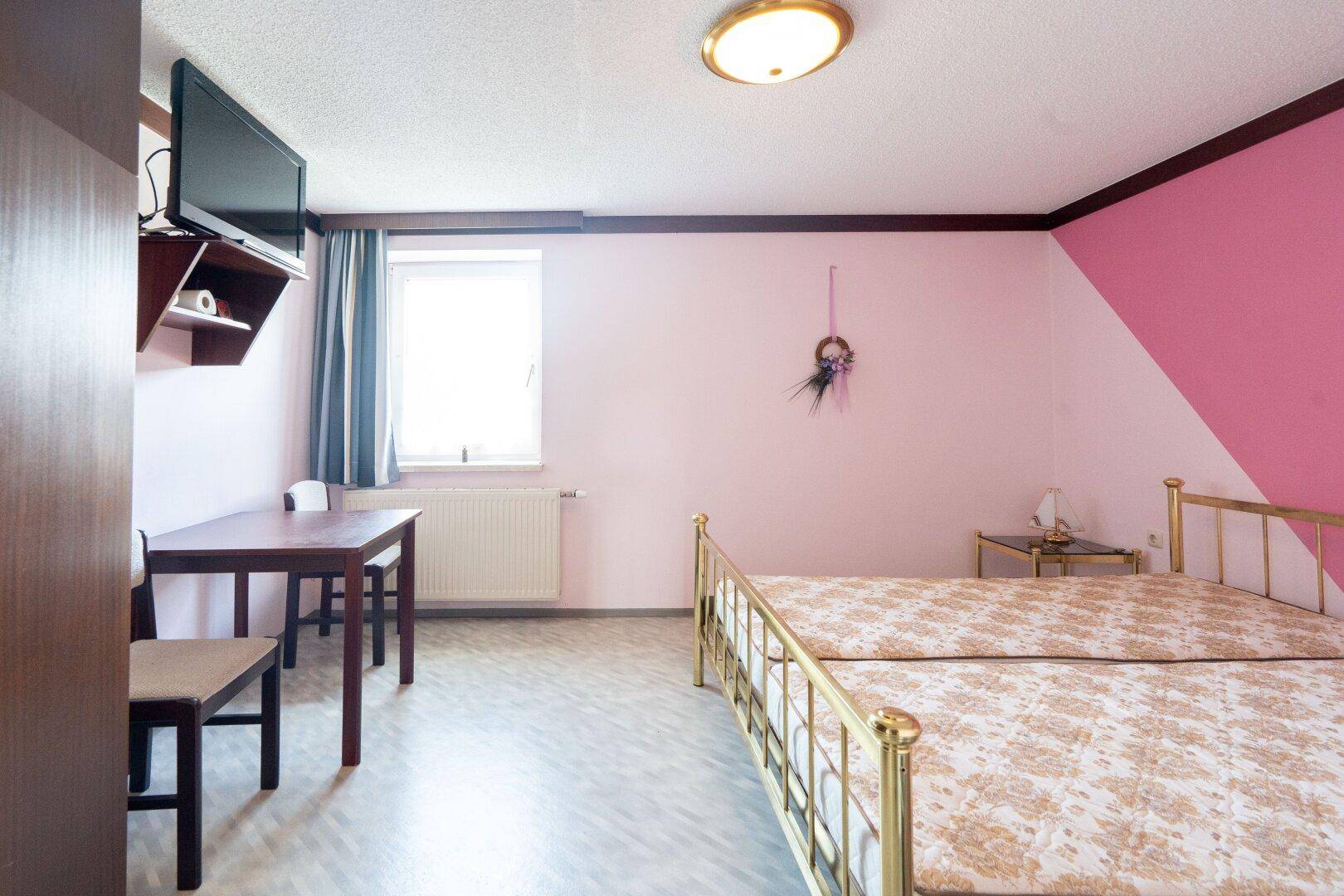 Farbiges Schlafzimmer mit zwei Einzelbetten, Tisch und Fernseher, hell und funktional.