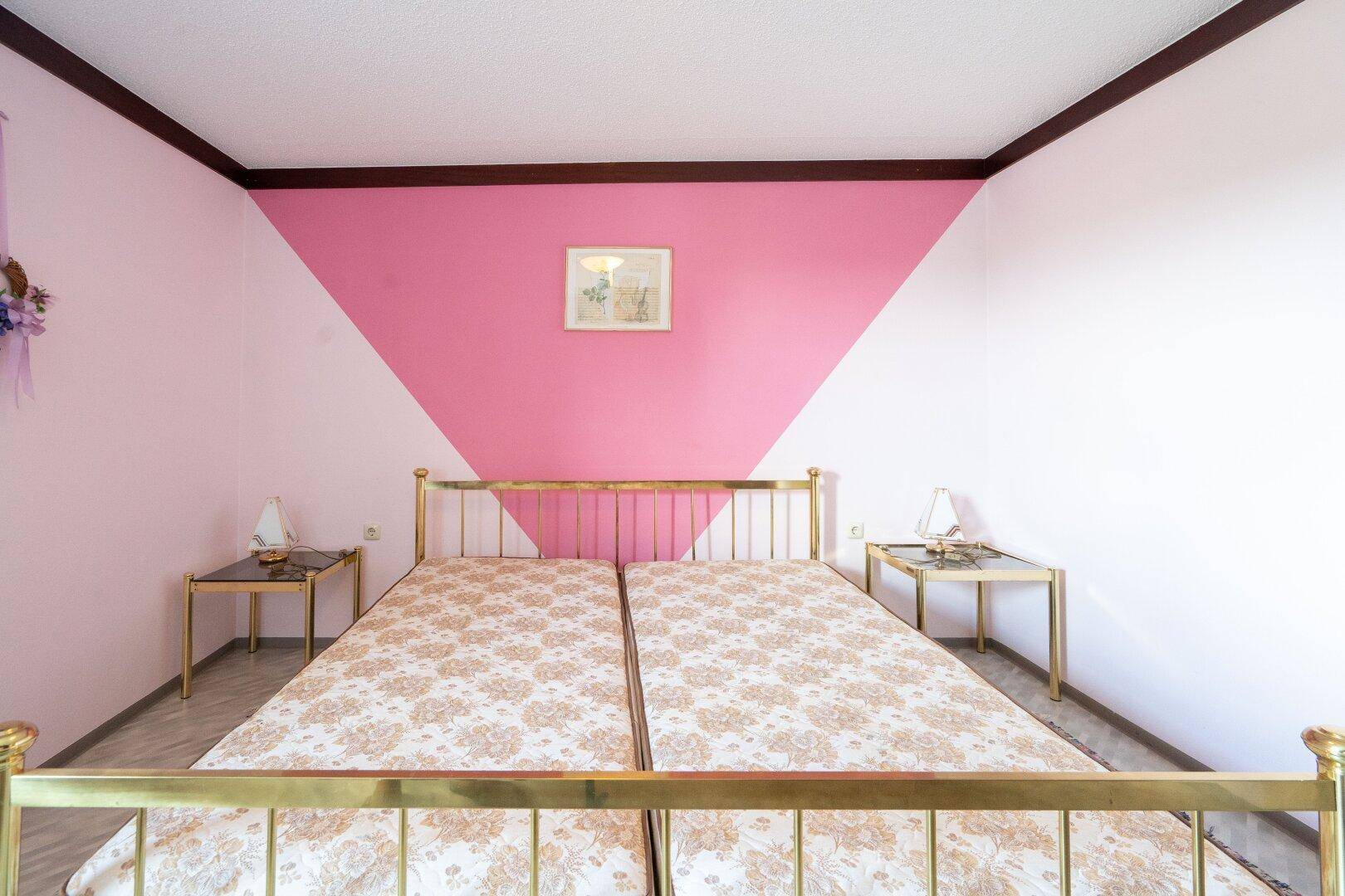 Schlafzimmer mit zwei Einzelbetten und auffälliger rosa Wandgestaltung, hell und einladend.