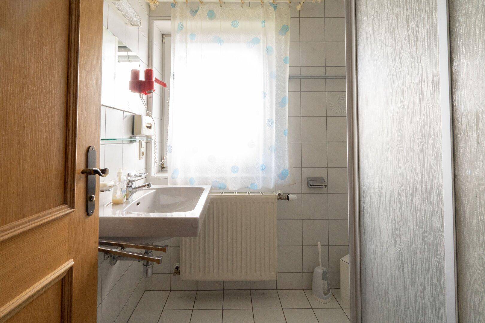 Helles Badezimmer mit Waschbecken, Duschkabine und Fenster, einfach und sauber.