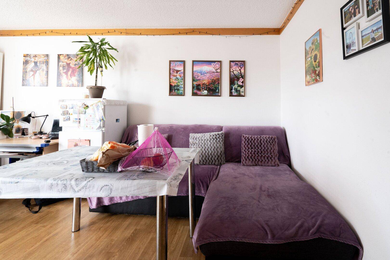 Gemütlicher Wohnbereich mit lila Sofa, Esstisch und Bildern an der Wand, hell und wohnlich.
