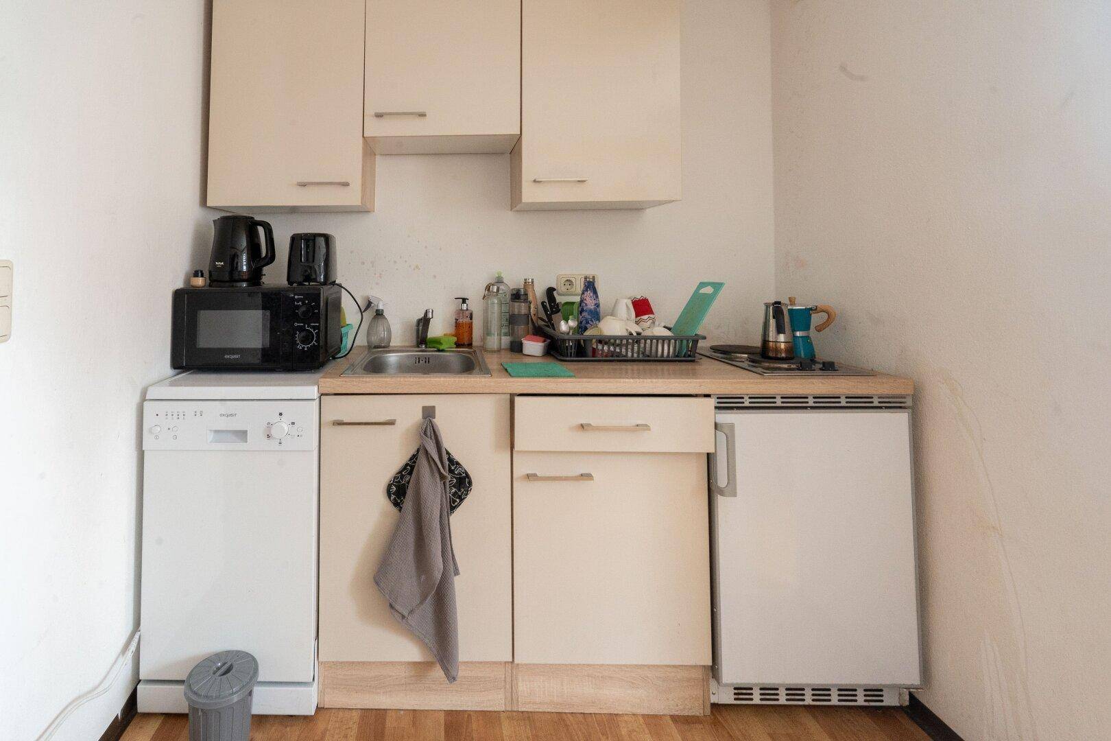 Kleine Küchenzeile mit Spüle, Mikrowelle und Kühlschrank, funktional und kompakt.
