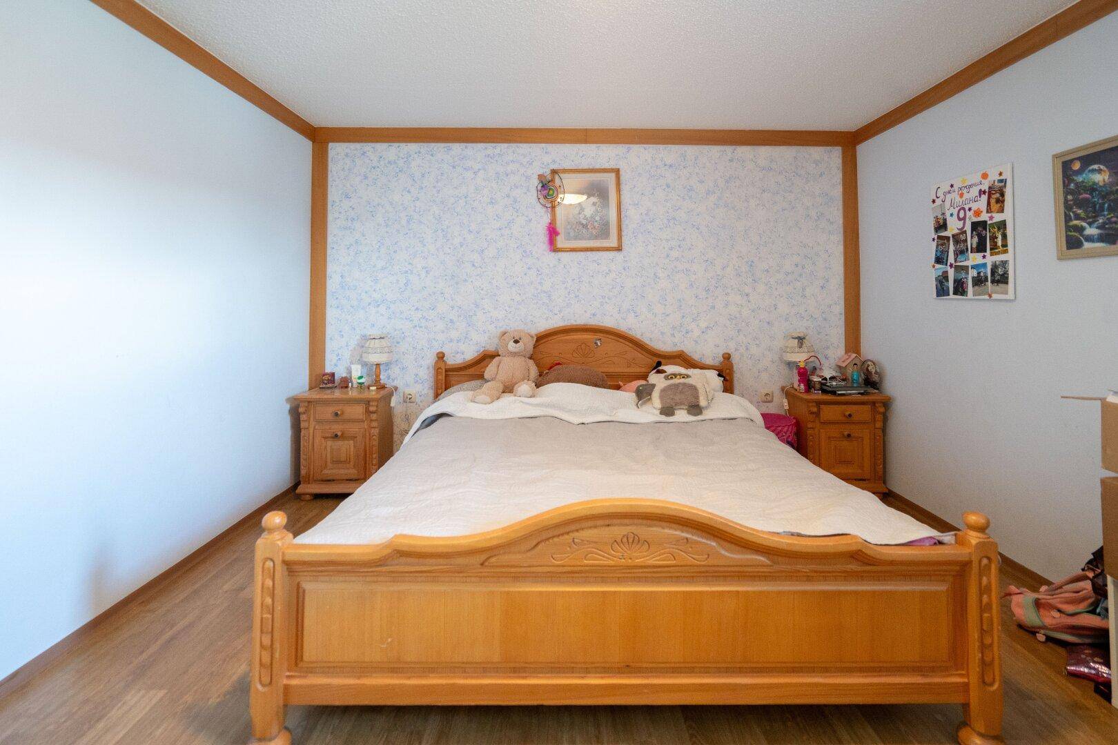 Schlafzimmer mit Holzbett, Nachttischen und gemusterter Tapete, umrahmt von Holzleisten.