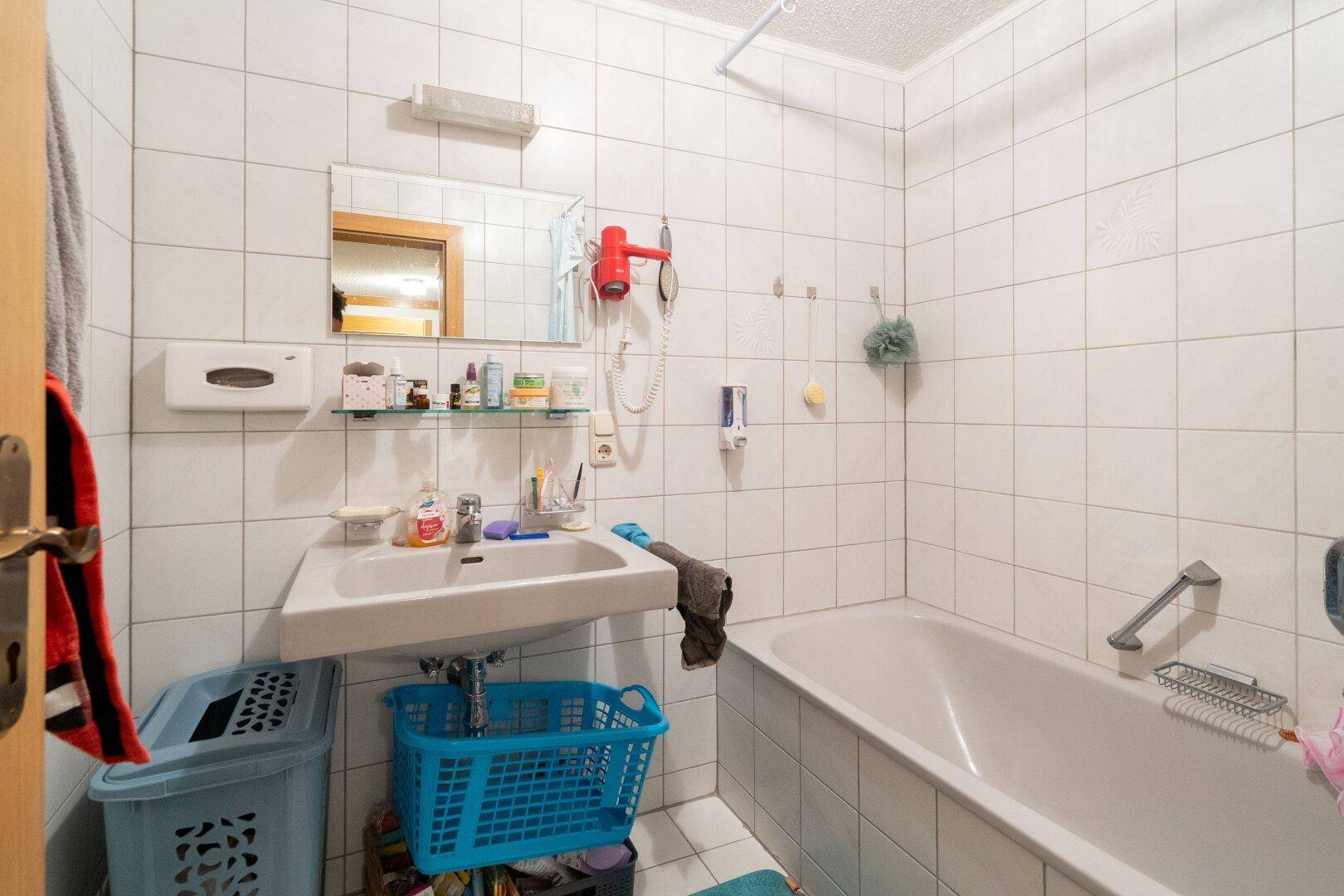 Gefliestes Badezimmer mit Badewanne, Waschbecken und Spiegel, in einem funktionalen Stil.