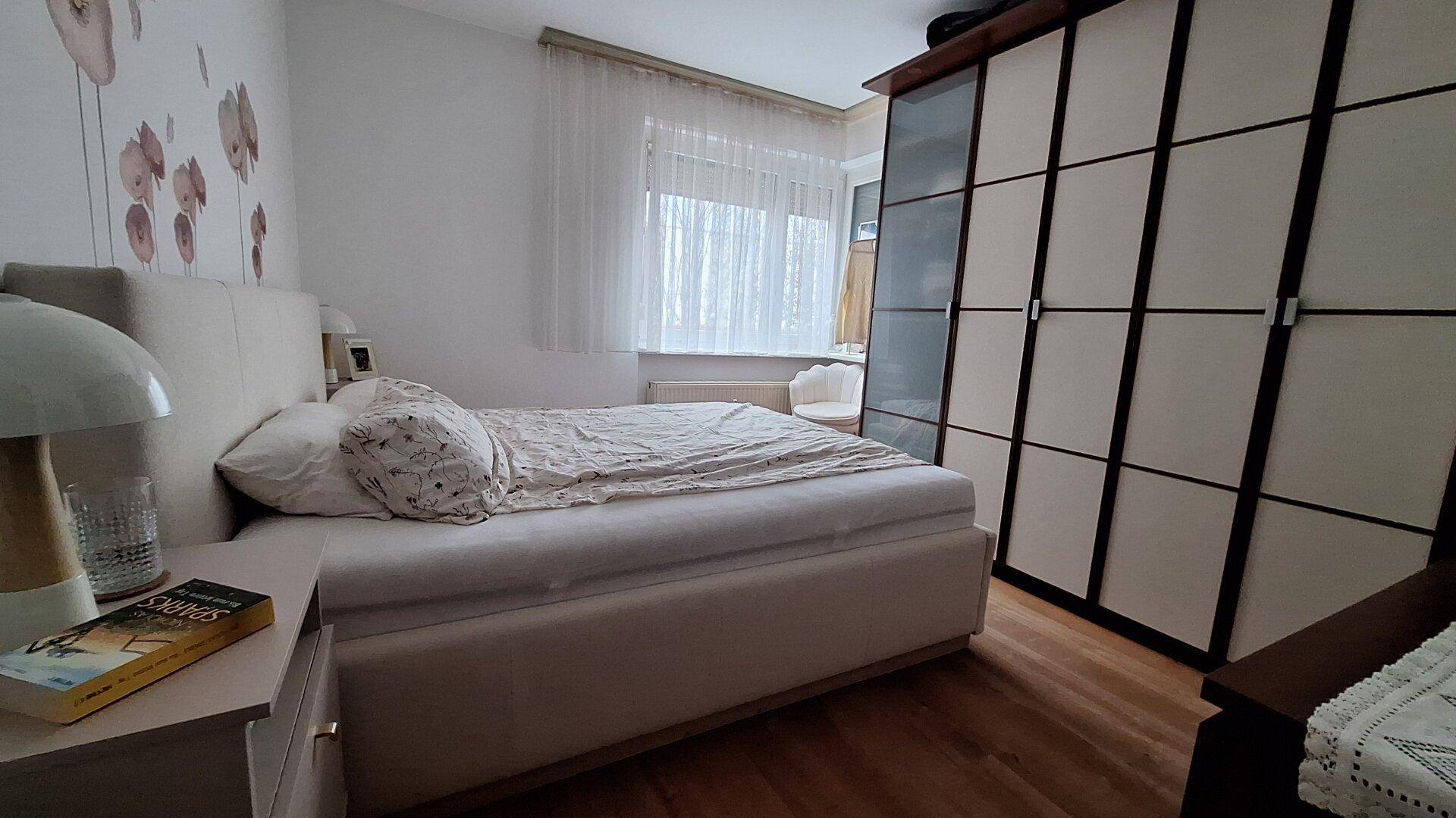 Gemütliches Schlafzimmer mit großem Bett, geräumigem Kleiderschrank und Fenster mit hellen Vorhängen.