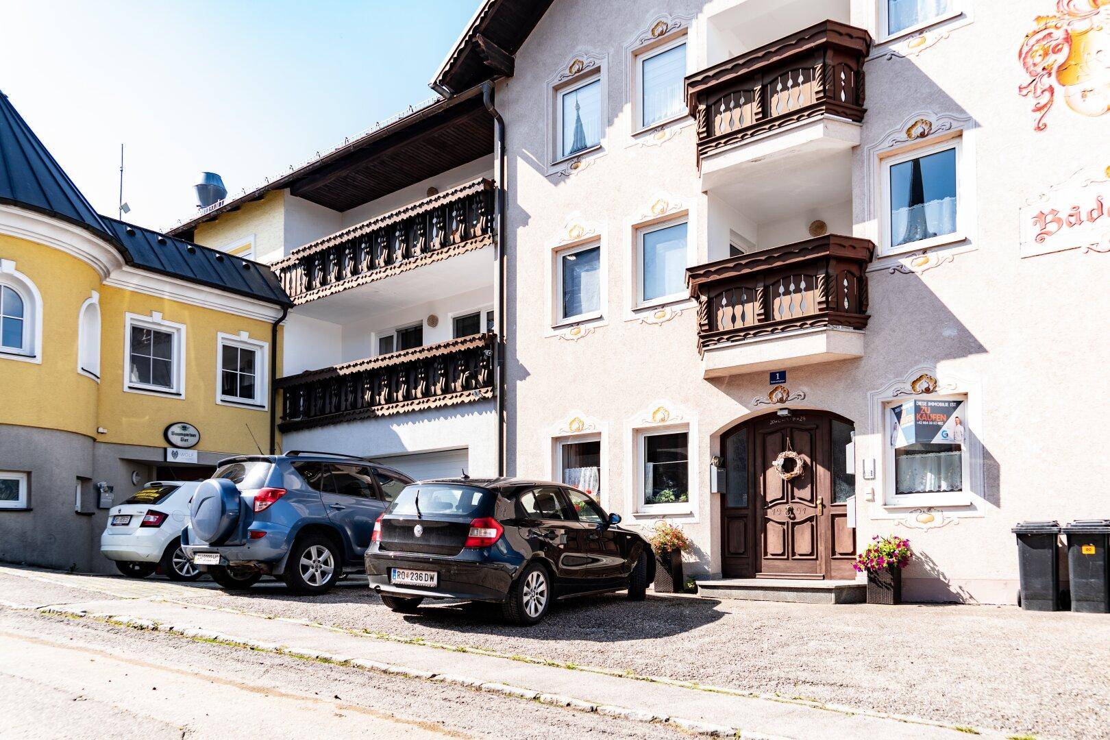 Nahaufnahme der traditionellen Fassade mit Holzbalkonen und geparkten Fahrzeugen vor dem Eingang.