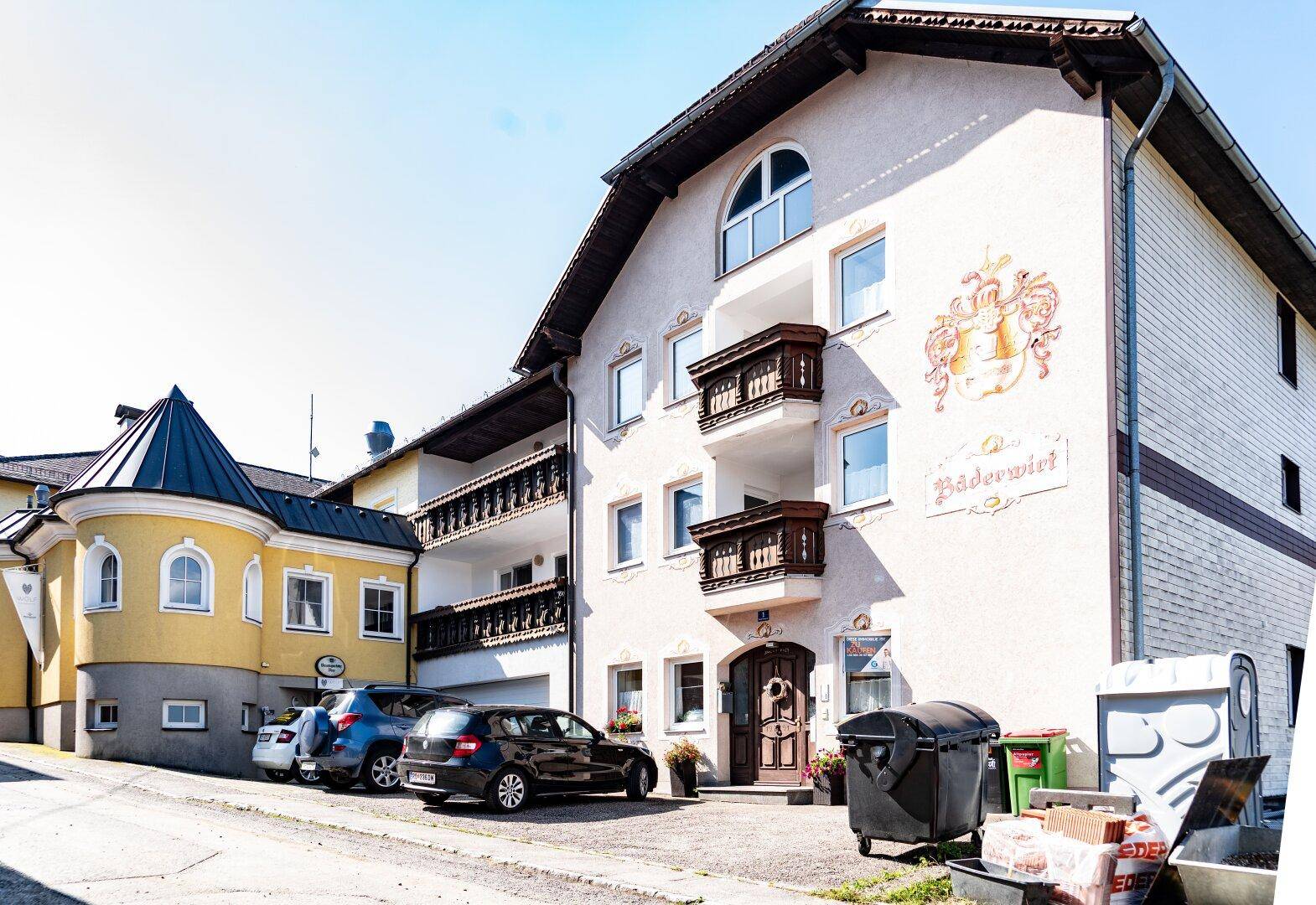 Traditionelles Gebäude mit bemalter Fassade, Holzbalkonen und geparkten Autos davor.