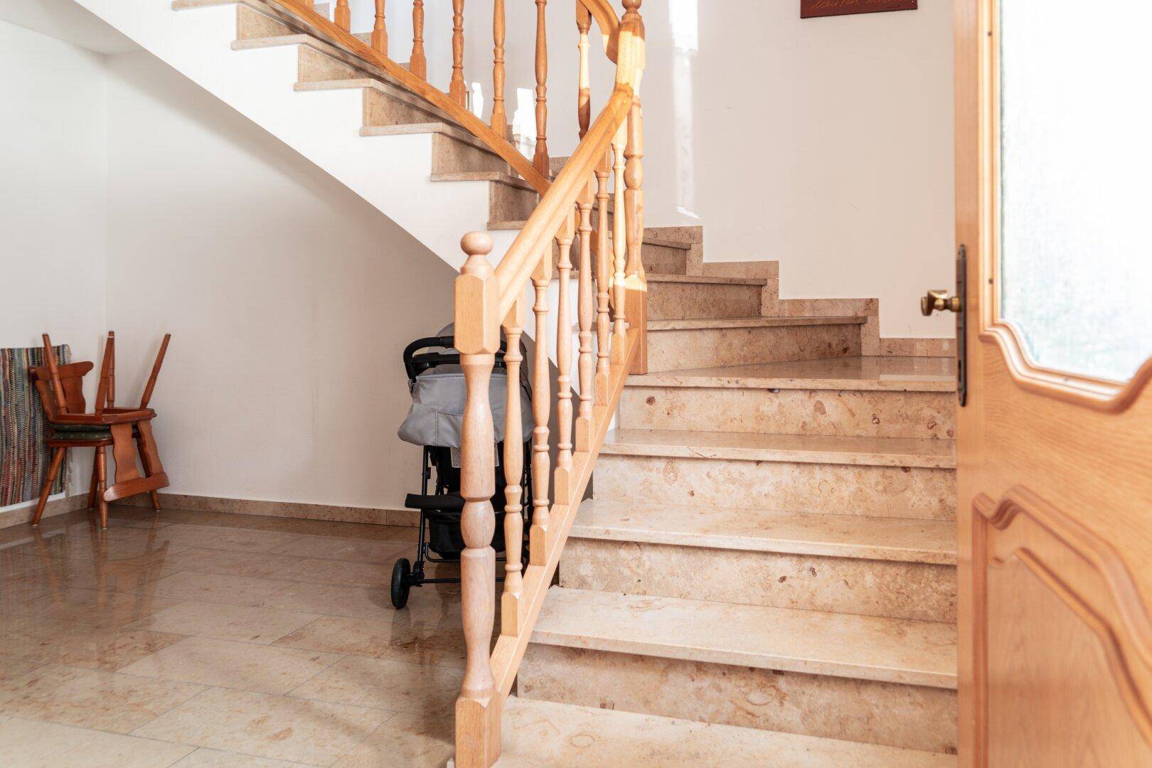 Heller Flur mit Marmorfliesen und einer Holztreppe mit gedrechseltem Geländer.