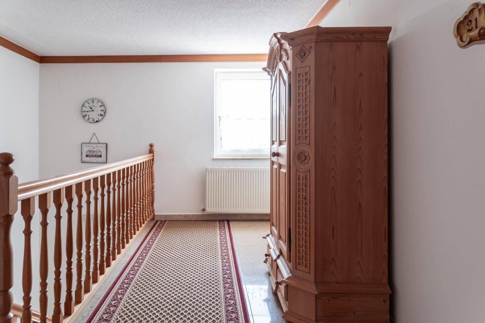 Oberer Flur mit Holzschrank, Teppichläufer und Fenster, das Tageslicht hereinlässt.