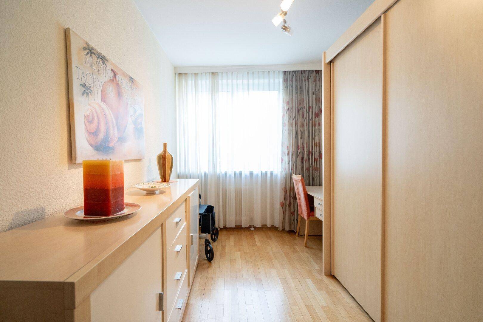 Heller Flur mit Holzfußboden, Schiebetüren und einem Fenster mit Vorhängen.