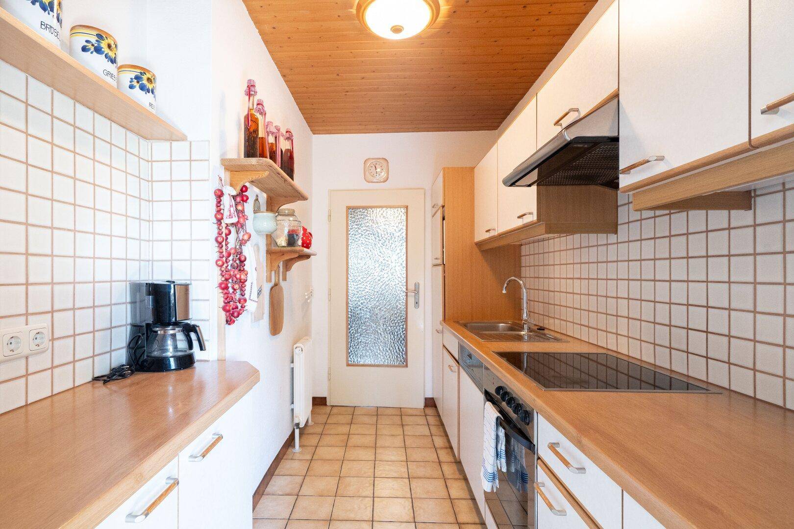 Funktionale Küche mit Holzdecke, weißen Schränken und Fliesenboden.