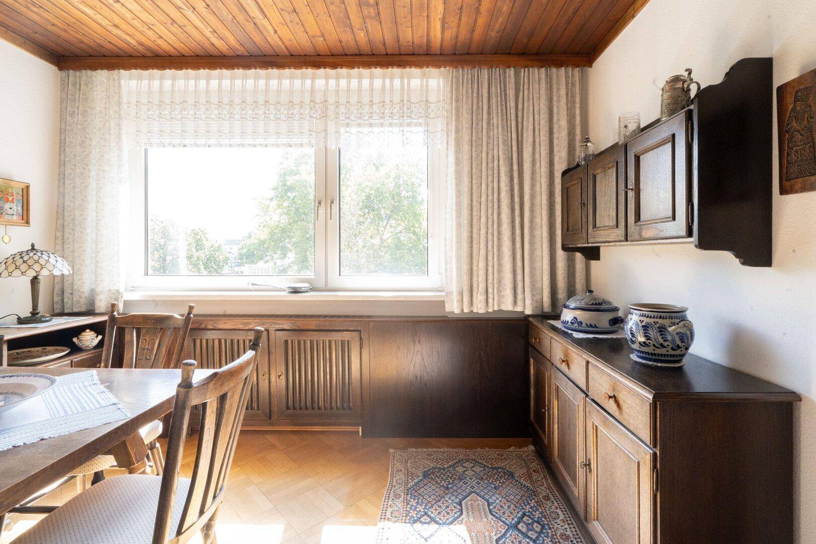 Esszimmer mit Holztisch, Stühlen und einem großen Fenster mit Blick ins Grüne.