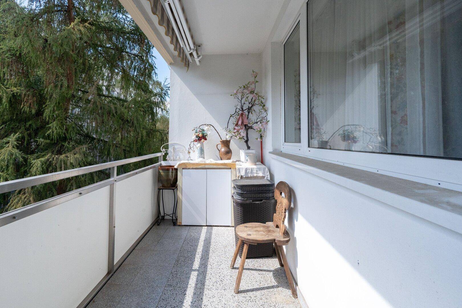 Sonniger Balkon mit Markise, Fliesenboden und Blick auf Bäume.