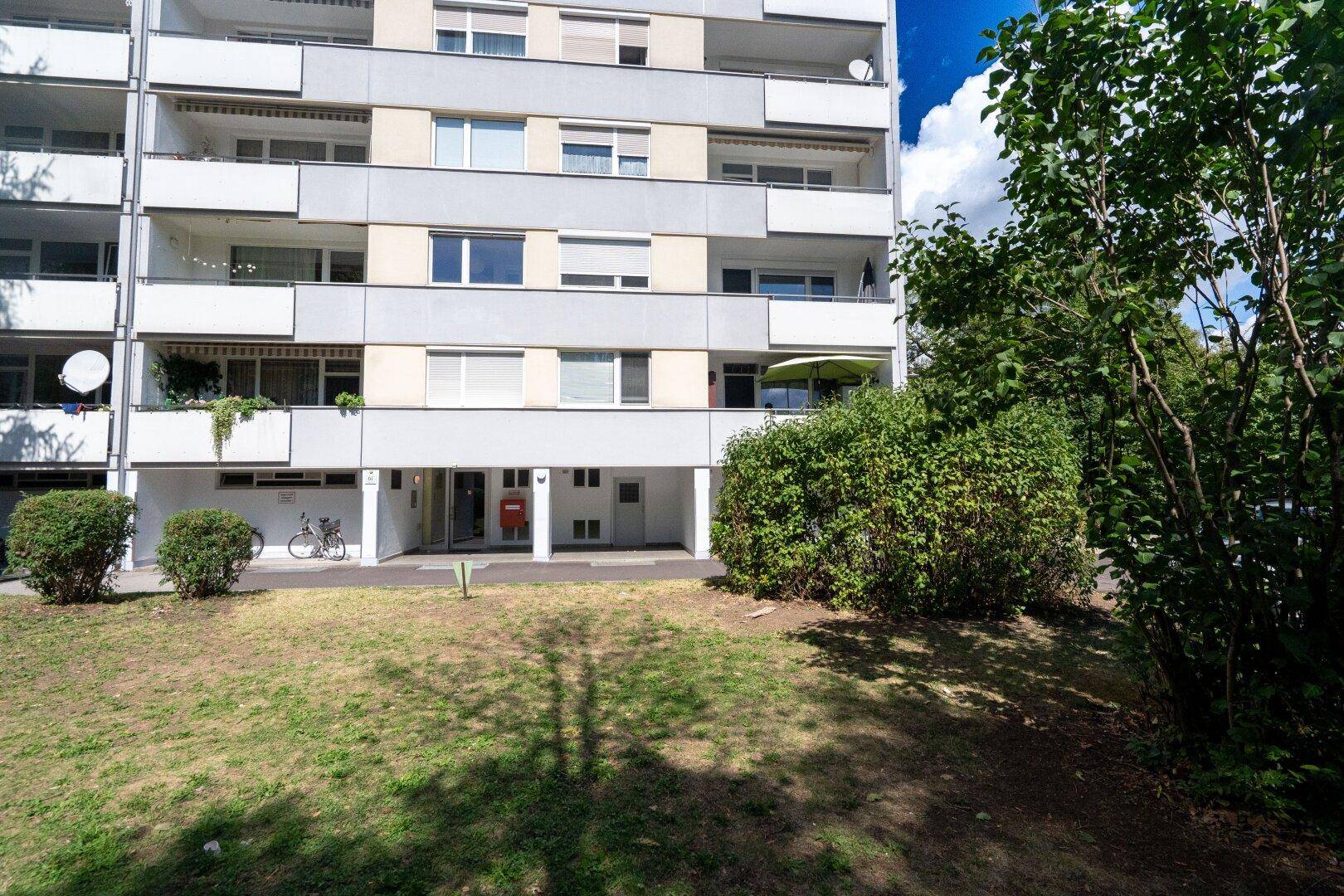 Mehrfamilienhaus mit Balkonen, Grünflächen und Parkplätzen.