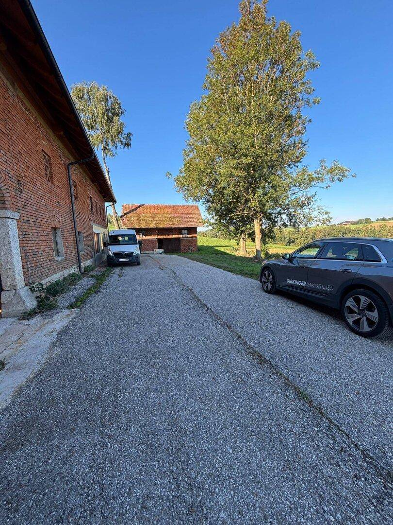 Weitläufige Schotterzufahrt vor einem alten Backsteingebäude, mit einem geparkten Auto und ländlicher Umgebung.