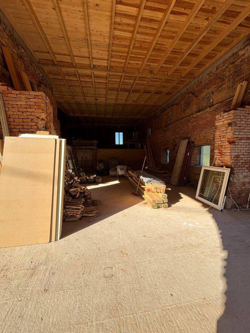 Geräumiger Lagerbereich mit Holzbalkendecke und Ziegelwänden, ideal für die Aufbewahrung von Materialien.