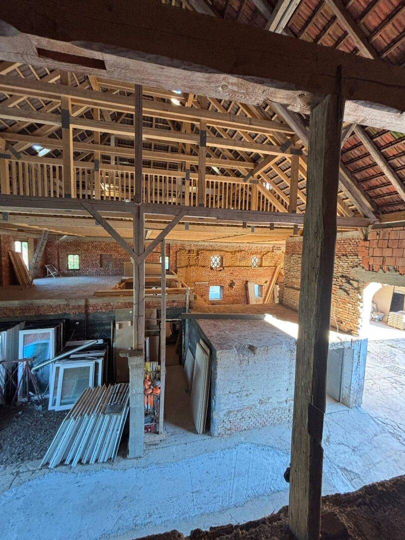 Innenansicht einer Scheune mit neu errichteter Holzempore und gelagerten Baumaterialien im unteren Bereich.