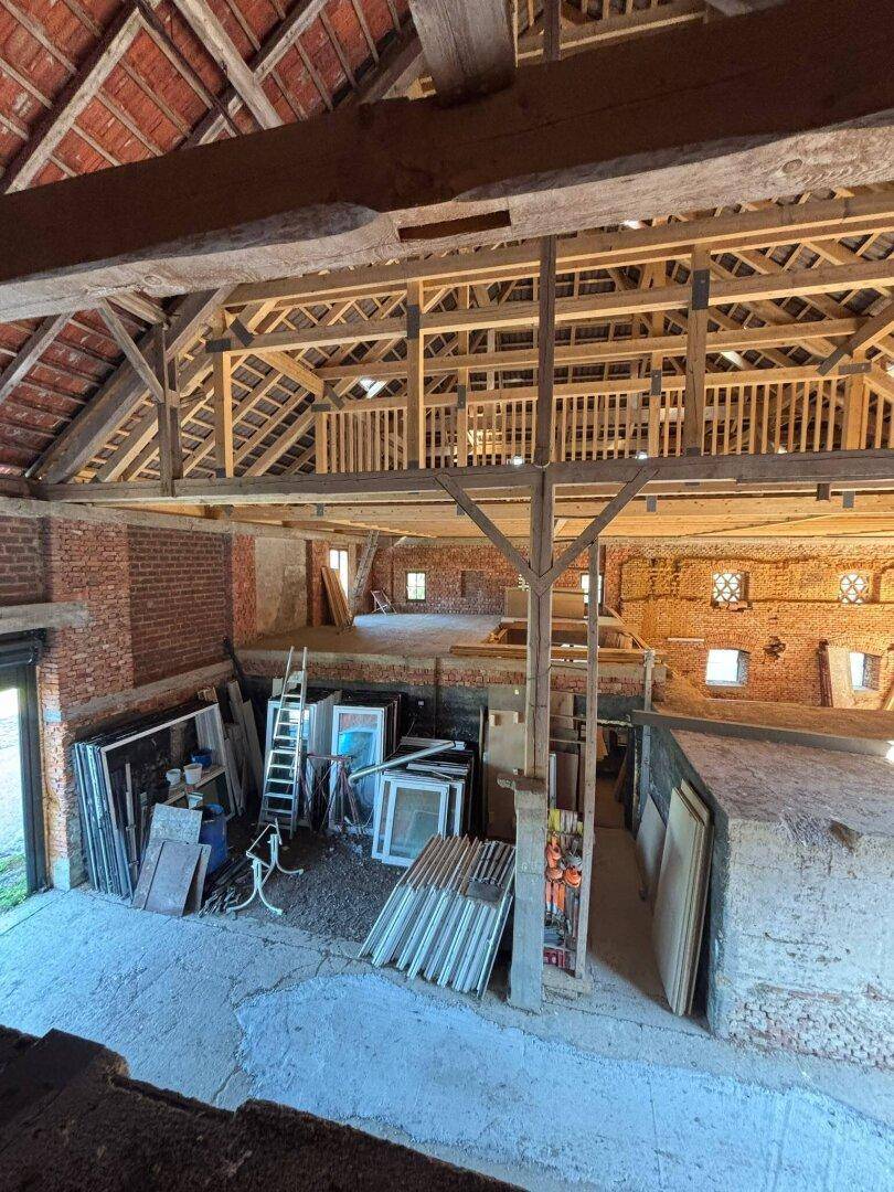 Weitläufiger Innenraum einer Scheune mit neuer Holzkonstruktion und gelagerten Baumaterialien, viel Tageslicht.