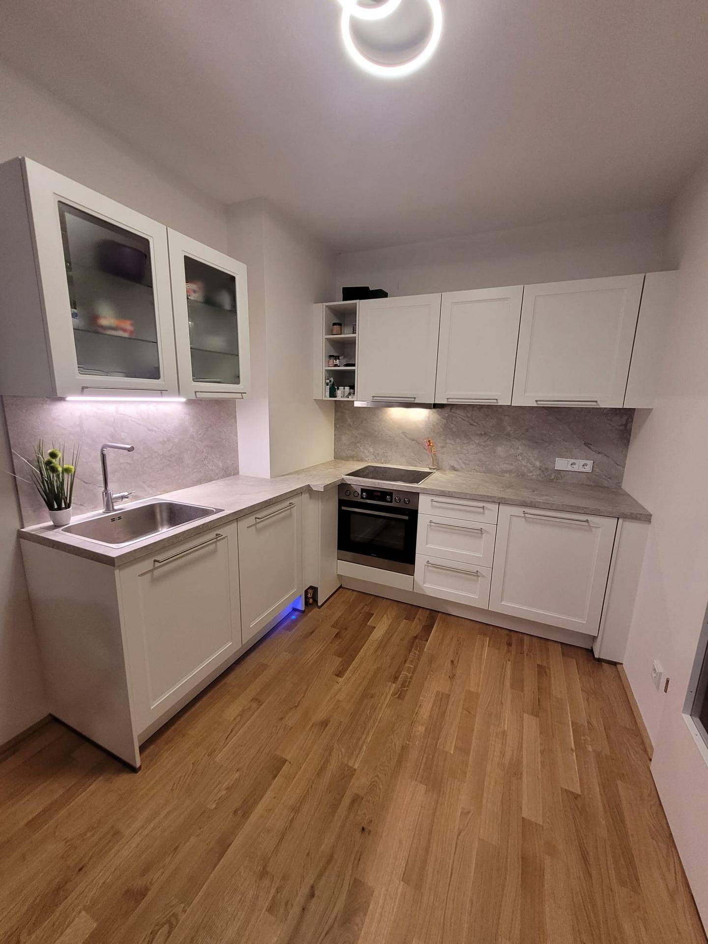 Moderne weiße Küche mit Holzboden, Einbaugeräten und ausreichend Stauraum.
