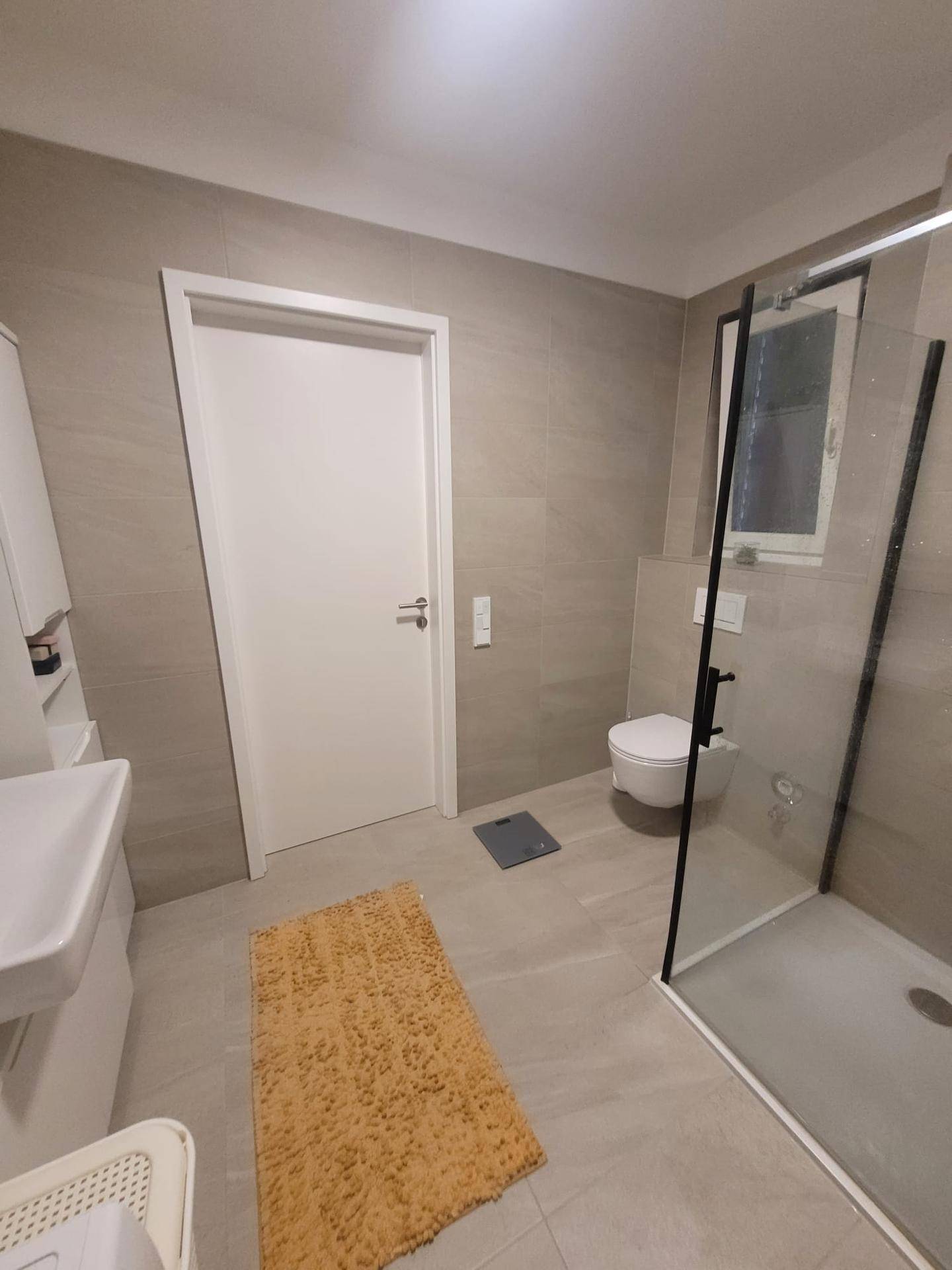 Modernes Badezimmer mit grauen Fliesen, wandhängendem WC und einer geräumigen begehbaren Dusche.