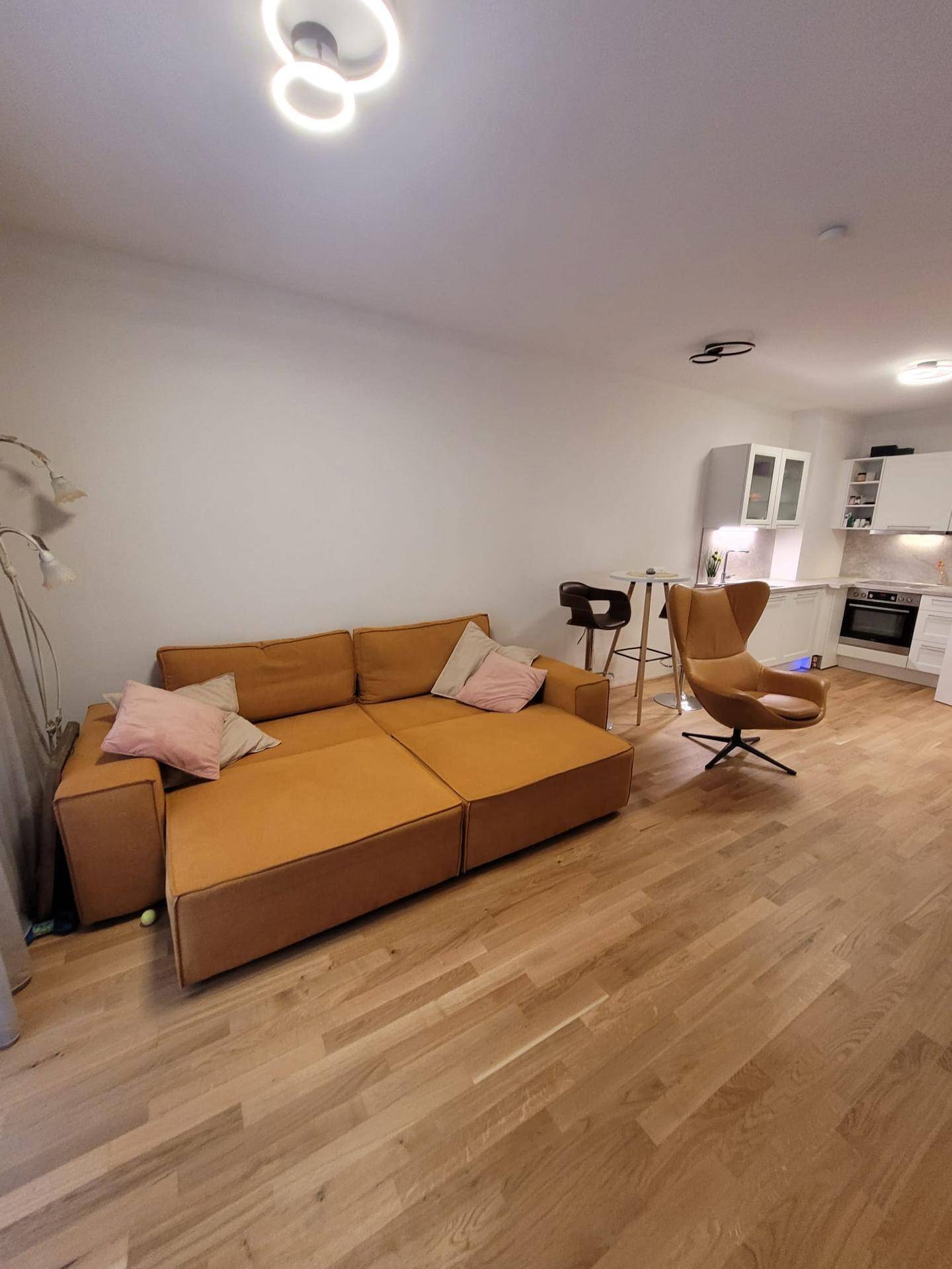 Offener Wohnbereich mit orangefarbenem Sofa und integrierter moderner Küche im Hintergrund.