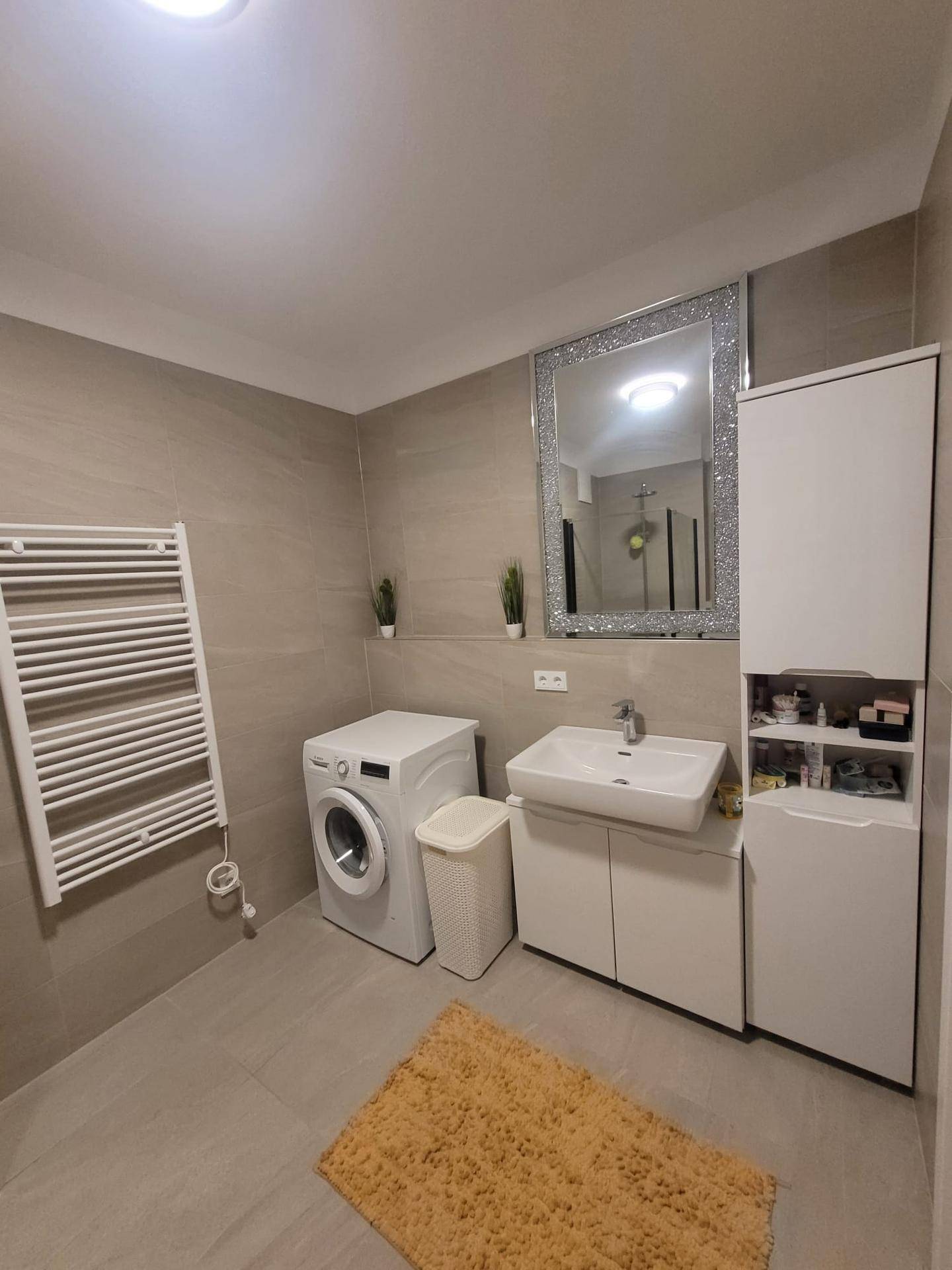 Funktionales Badezimmer mit Waschbecken, Spiegelschrank, Waschmaschine und beheiztem Handtuchhalter.