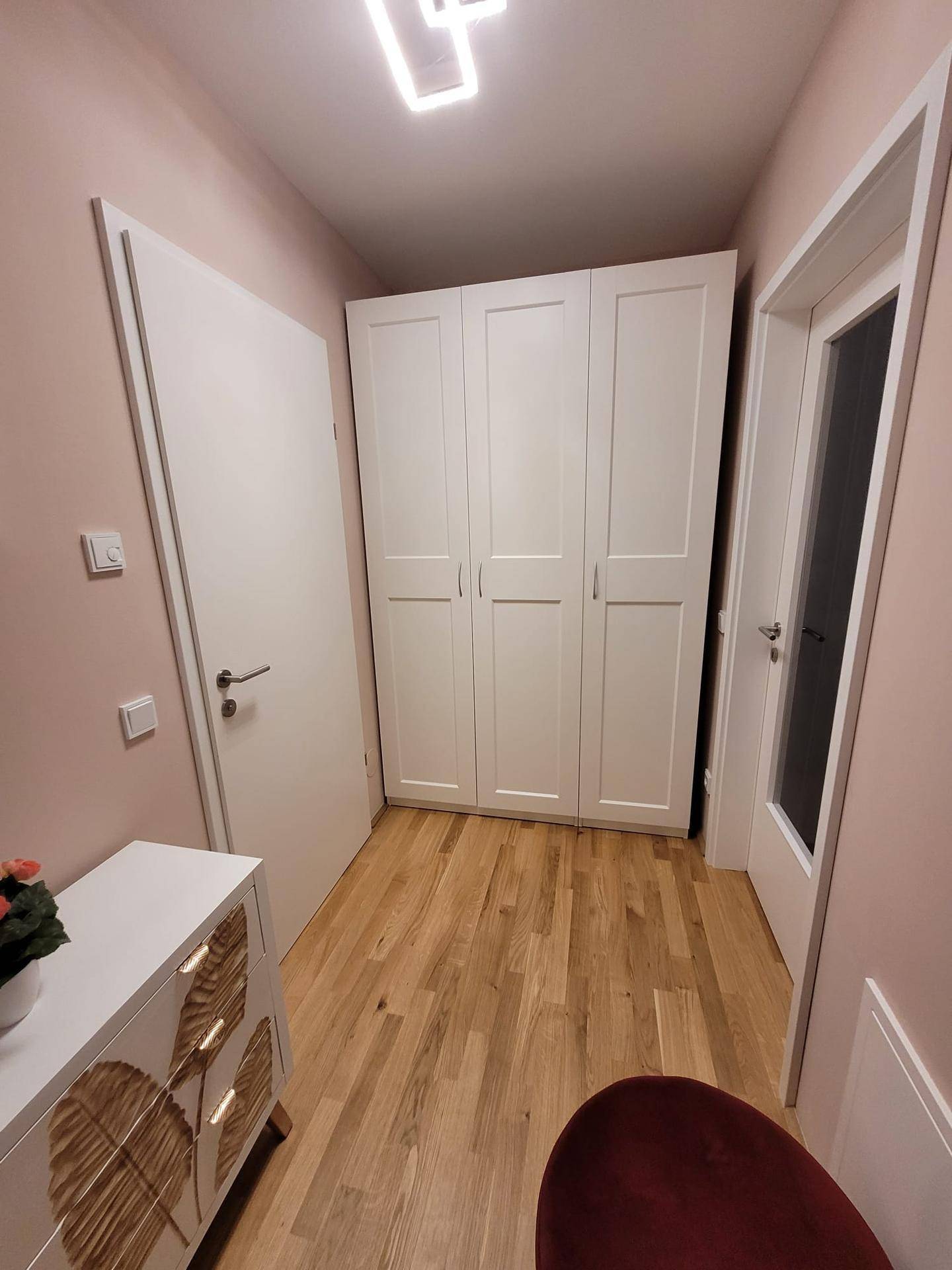 Heller Flur mit weißem Kleiderschrank, Holzboden und einer modernen Deckenleuchte.