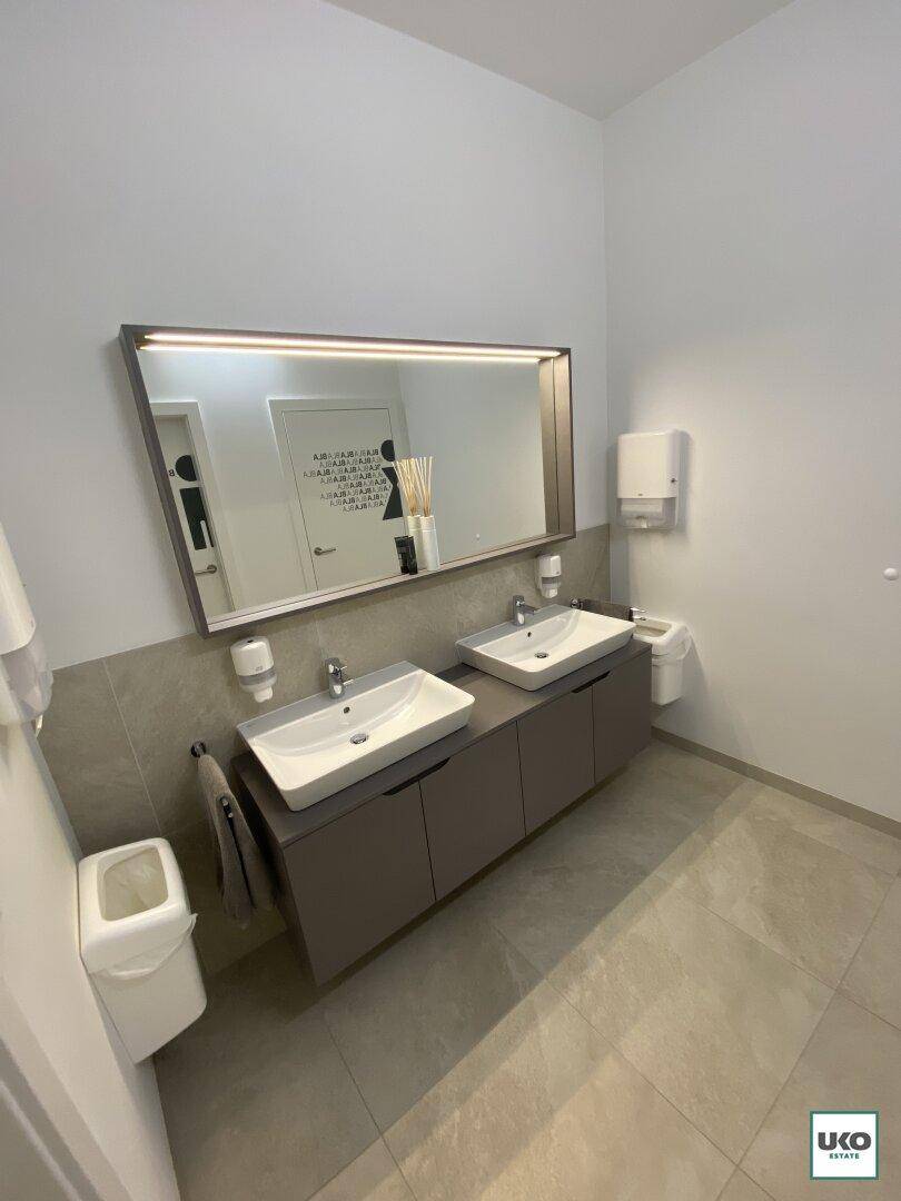 Modernes WC mit zwei Waschbecken, großem Spiegel und hellen Fliesen, funktional und sauber.