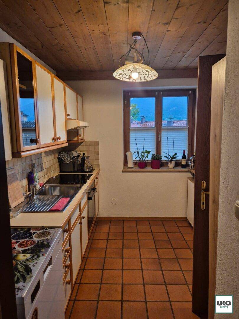 Funktionale Küche mit Holzschränken, Terrakotta-Fliesenboden und Fenster mit Bergblick.