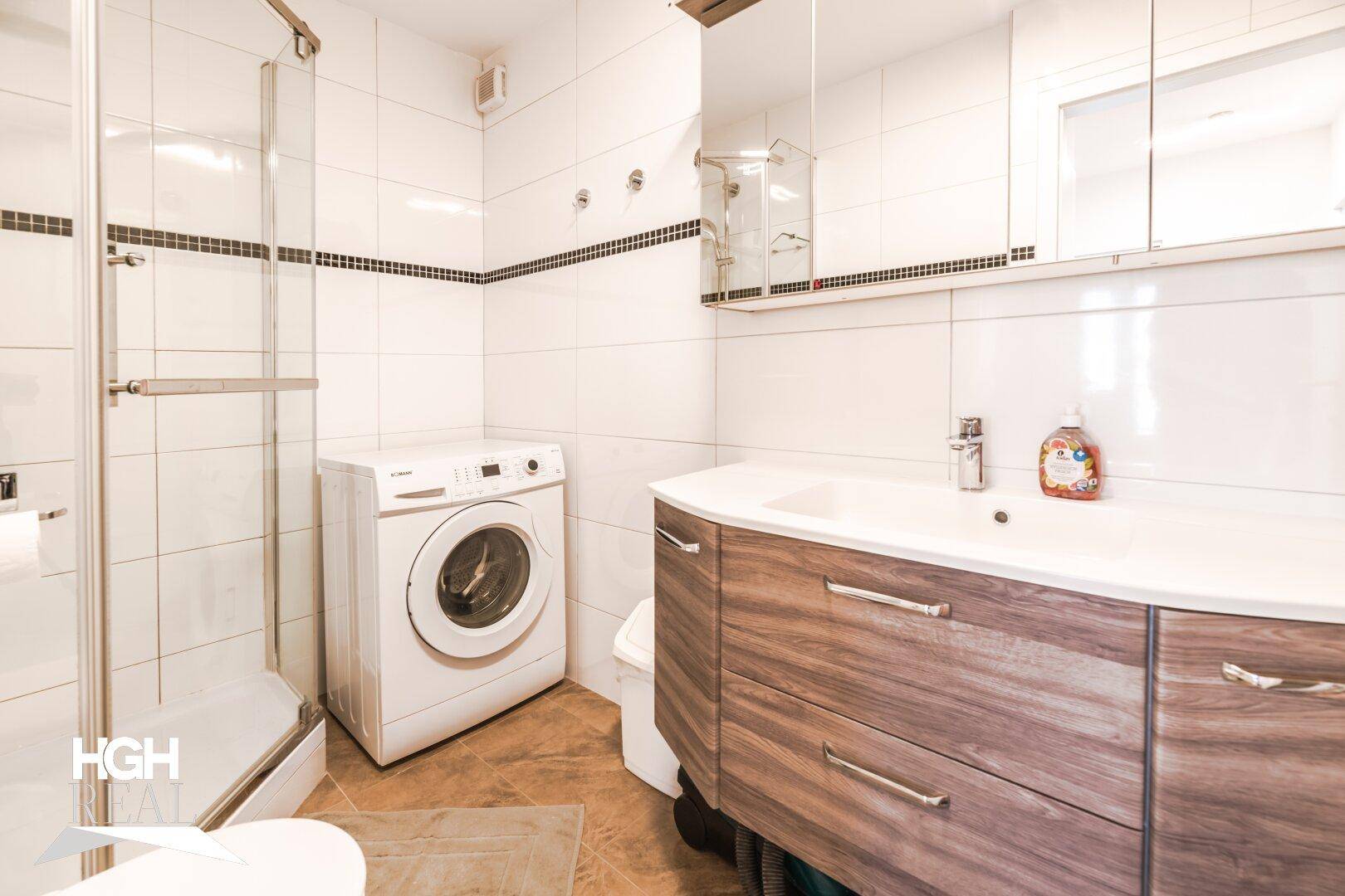 Funktionales Badezimmer mit Dusche, Waschbeckenunterschrank und integrierter Waschmaschine.