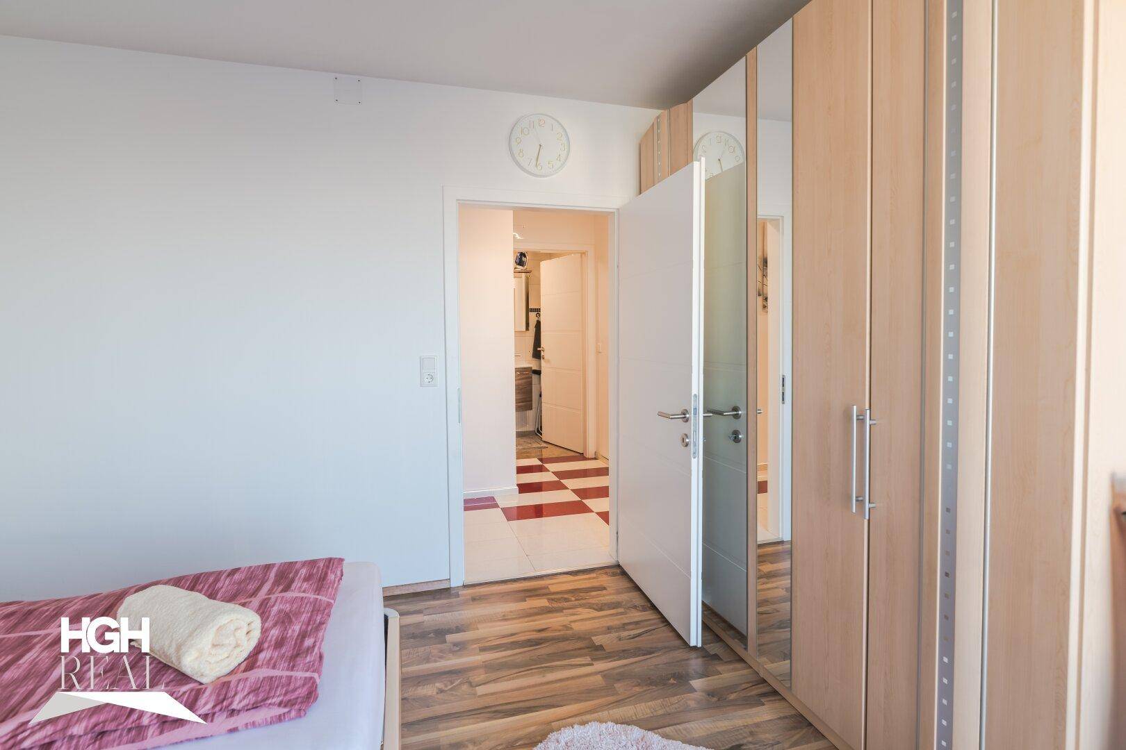Schlafzimmer mit hellem Holzschrank und Blick in einen angrenzenden Raum mit Fliesenboden.