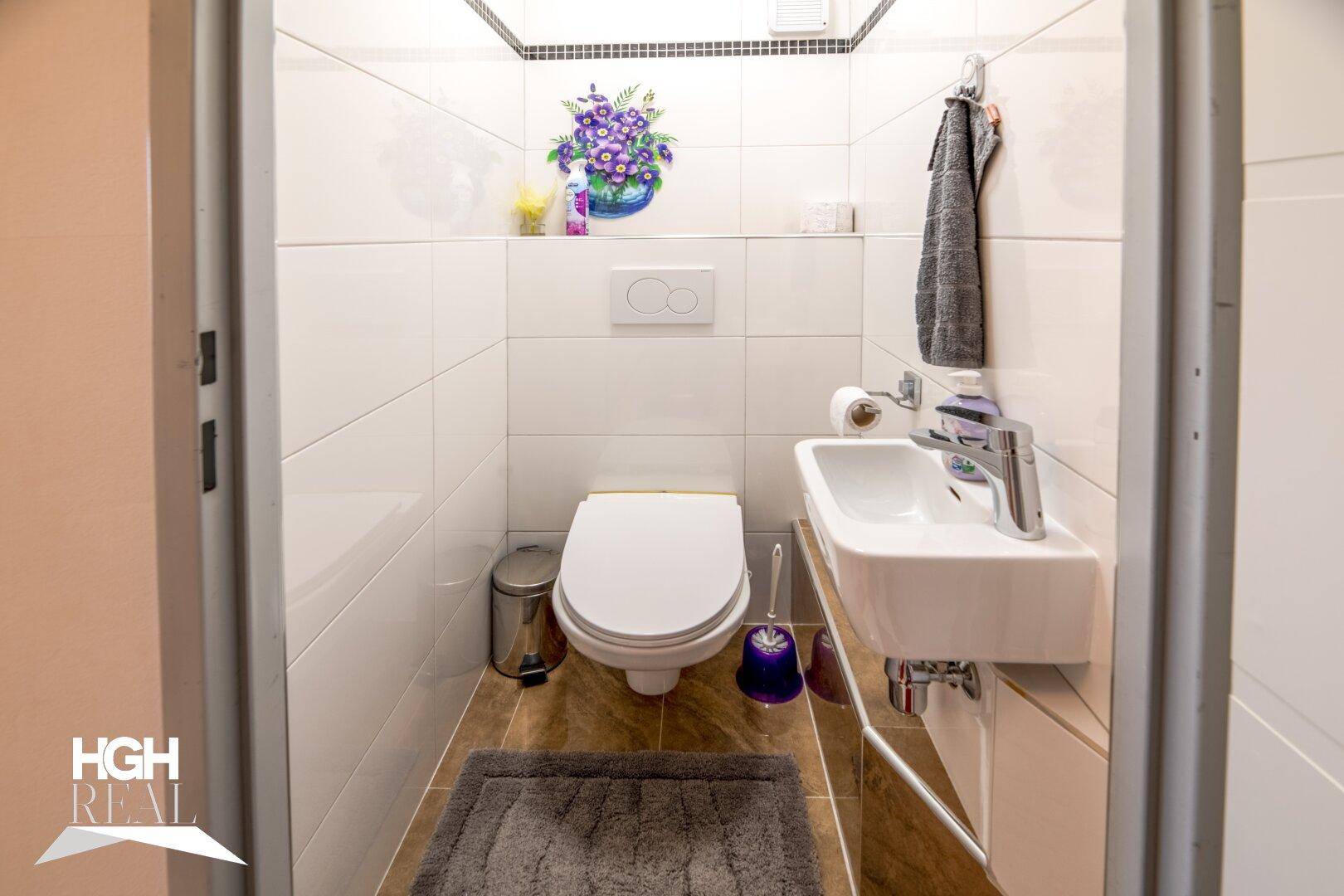 Kompaktes Gäste-WC mit Wand-WC, kleinem Waschbecken und Fliesenboden.