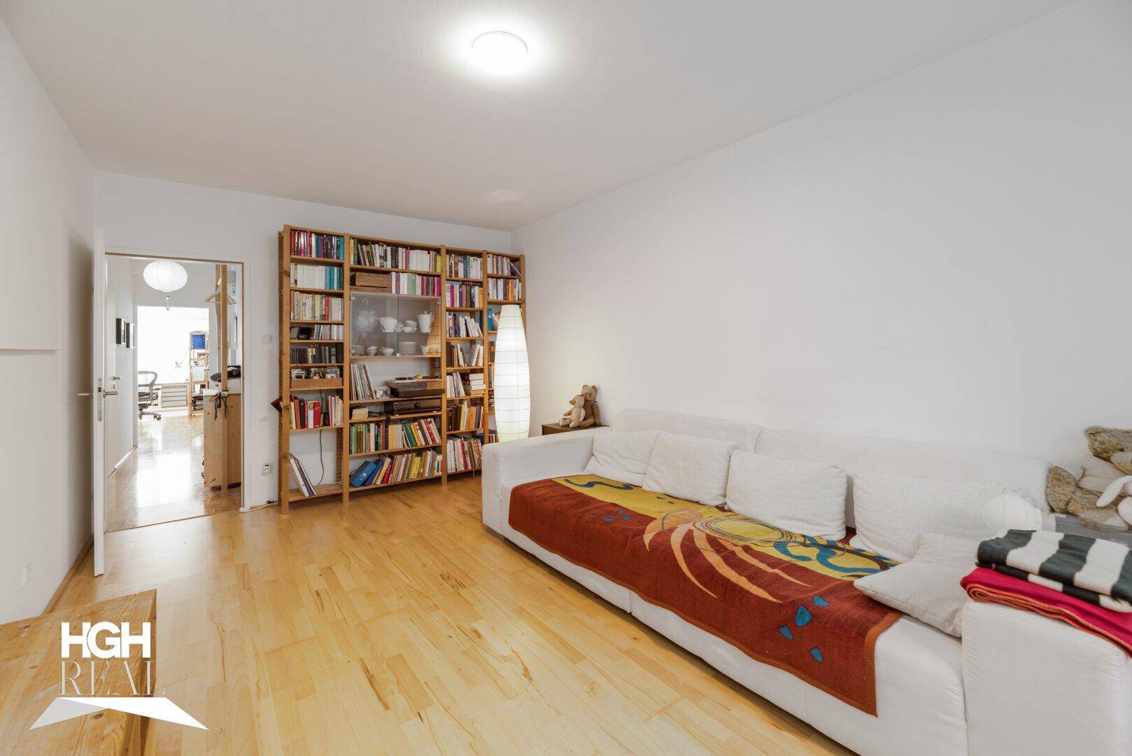 Helles Wohnzimmer mit weißem Sofa, großem Bücherregal und hellem Holzfußboden.