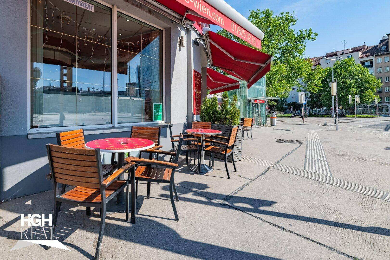 Außenbereich des Cafés mit Tischen und Stühlen auf dem Bürgersteig, umgeben von Stadtansicht.