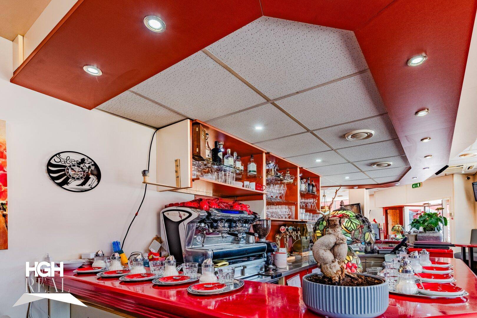 Blick auf die Bar mit gut bestückten Regalen voller Flaschen und Gläser, beleuchtet von Deckenstrahlern.