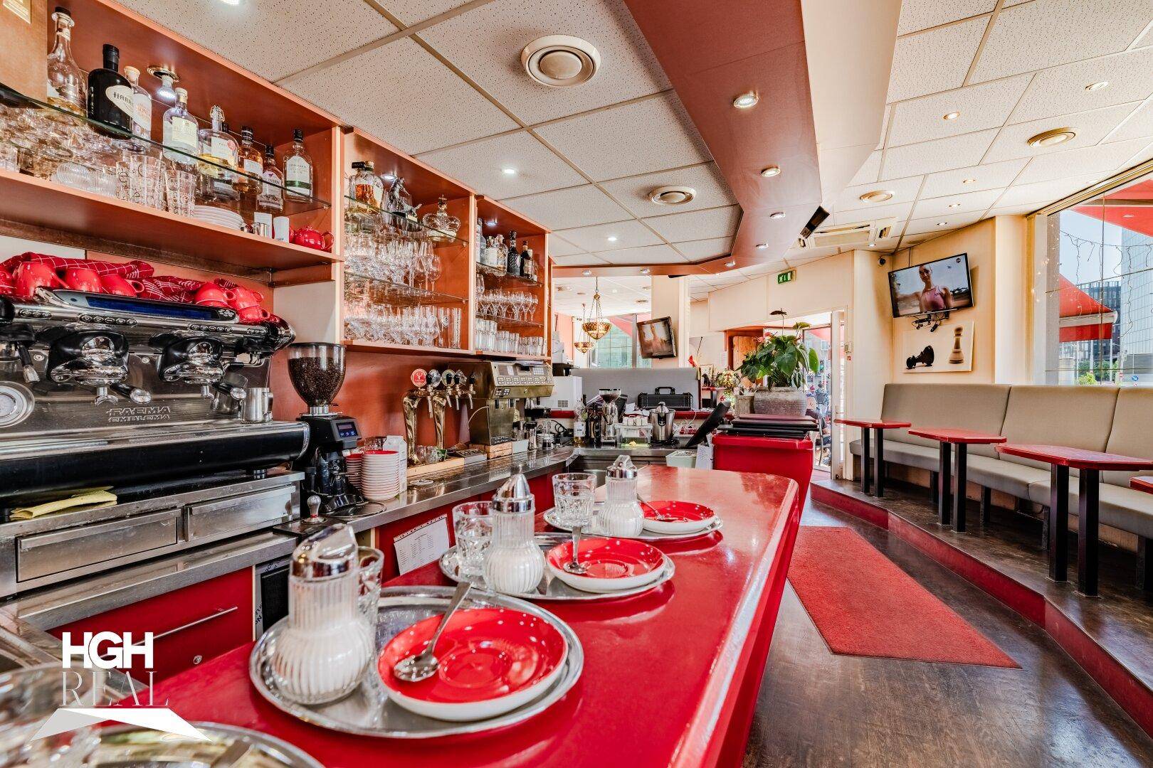Nahaufnahme der Bar mit professioneller Kaffeemaschine, Gläsern und Geschirr auf der roten Theke.