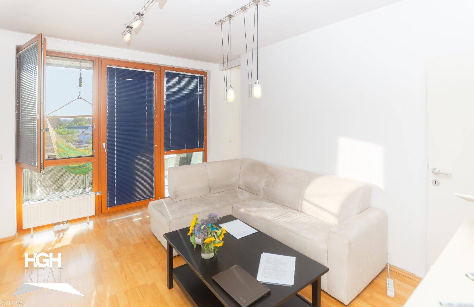 Lichtdurchflutetes Wohnzimmer mit beigem Ecksofa und Zugang zum Balkon.