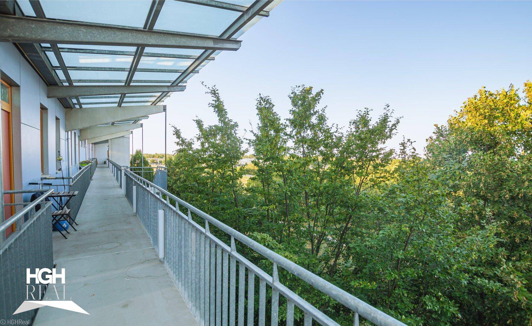 Langer überdachter Balkon mit Metallgeländer und weitem Blick ins Grüne.