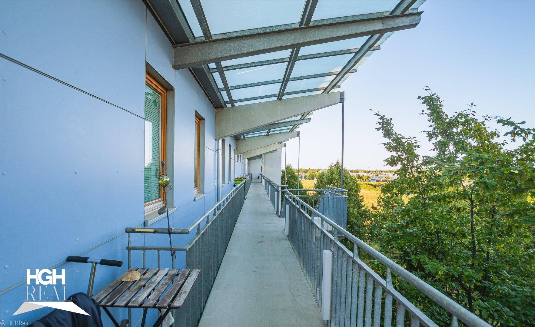 Überdachte Loggia mit blauer Fassade, Sitzgelegenheit und Blick auf die Landschaft.