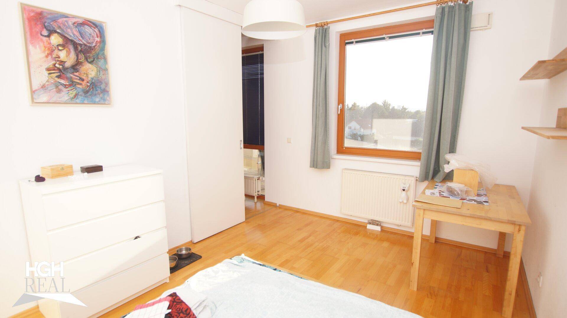 Schlafzimmer mit Holzboden, weißer Kommode und Fenster mit Ausblick.