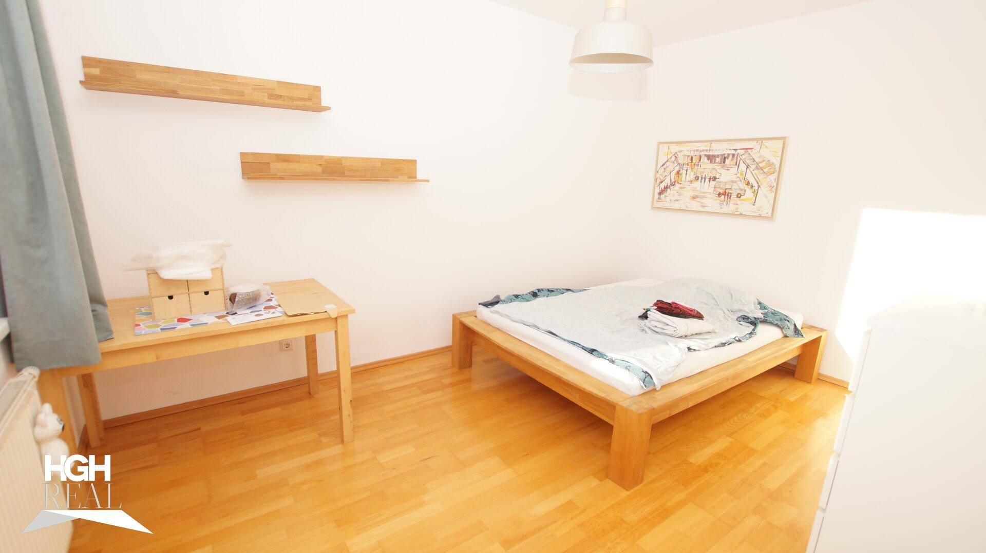 Helles Schlafzimmer mit Holzbett, Schreibtisch und Regalen an der Wand.